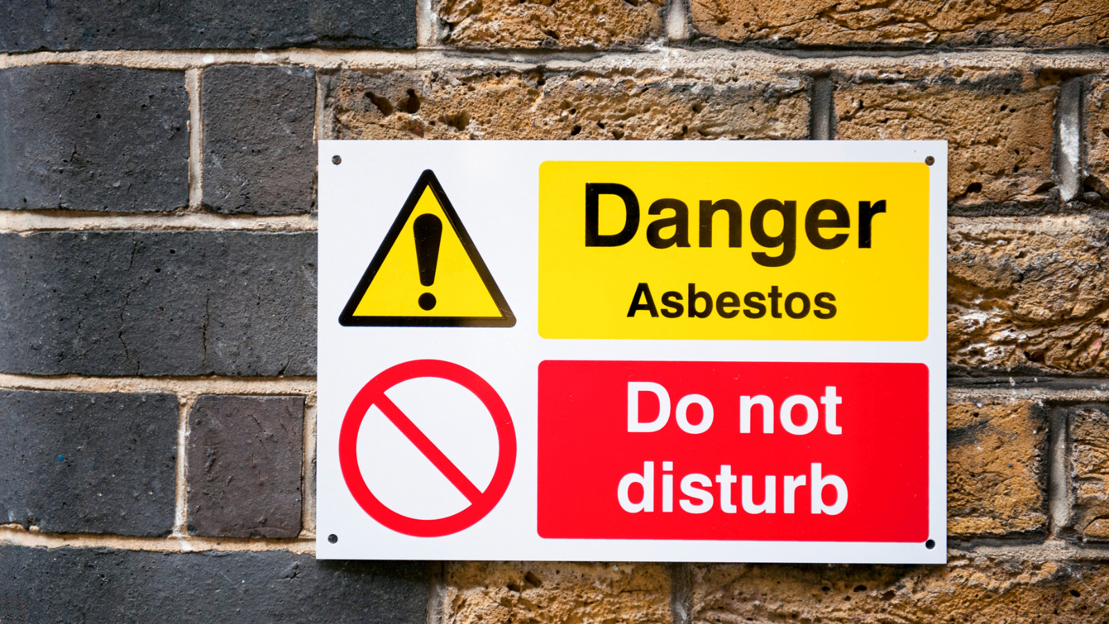 Asbestos risks warning sign on brick wall that reads: Danger Asbestos Do Not Disturb