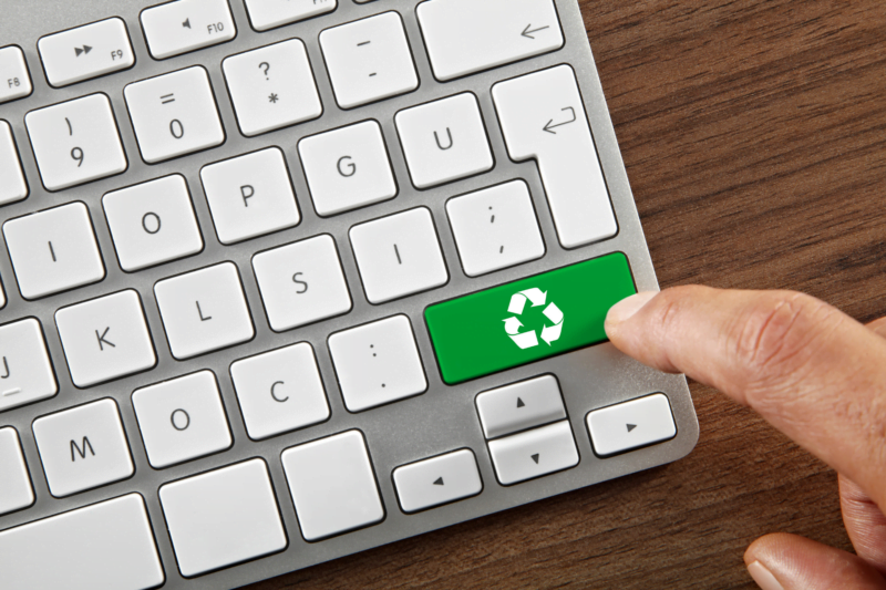 Finger pushing green button featuring recycling symbol on computer keyboard