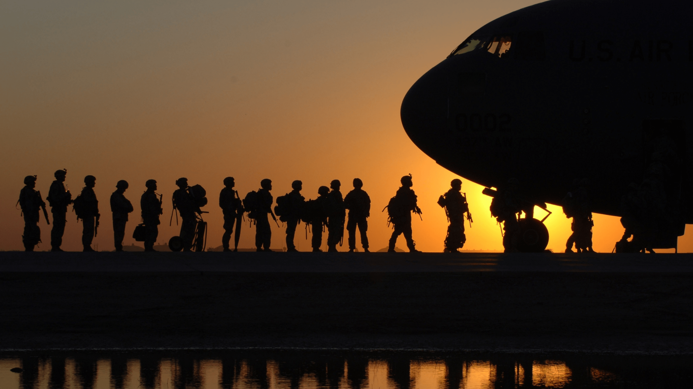 Silhouetted military personnel walking along a runway to an aeroplane at sunset