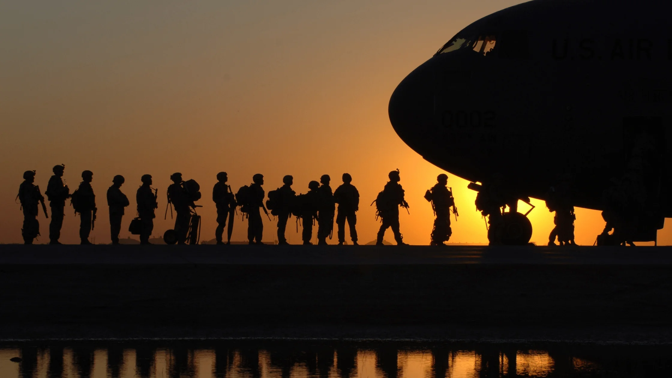 Silhouetted military personnel walking along a runway to an aeroplane at sunset