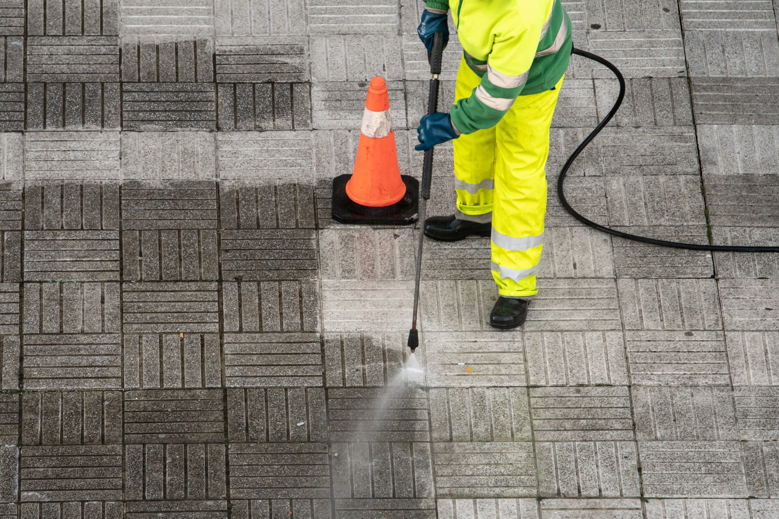 Community Cleaning - Worker cleaning the street sidewalk with high pressure water jet