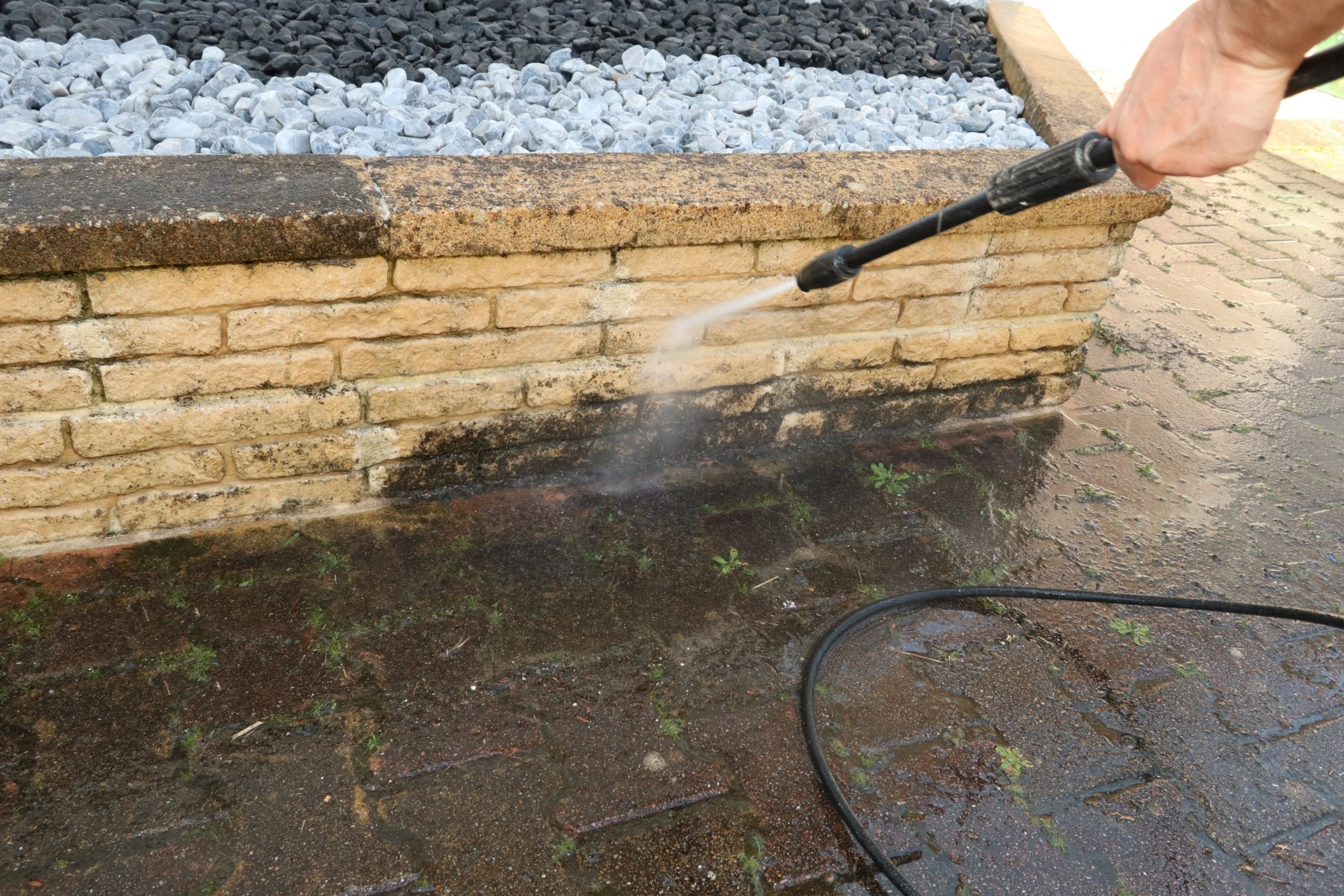 Man cleaning dirty walkway with high pressure water cleaner Outdoor Domestic Cleaning - man pressure washes brickwork