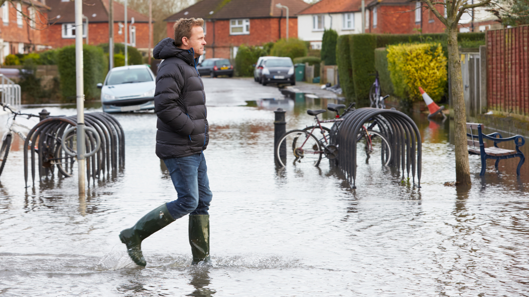 man in wellies walking along flooded urban street