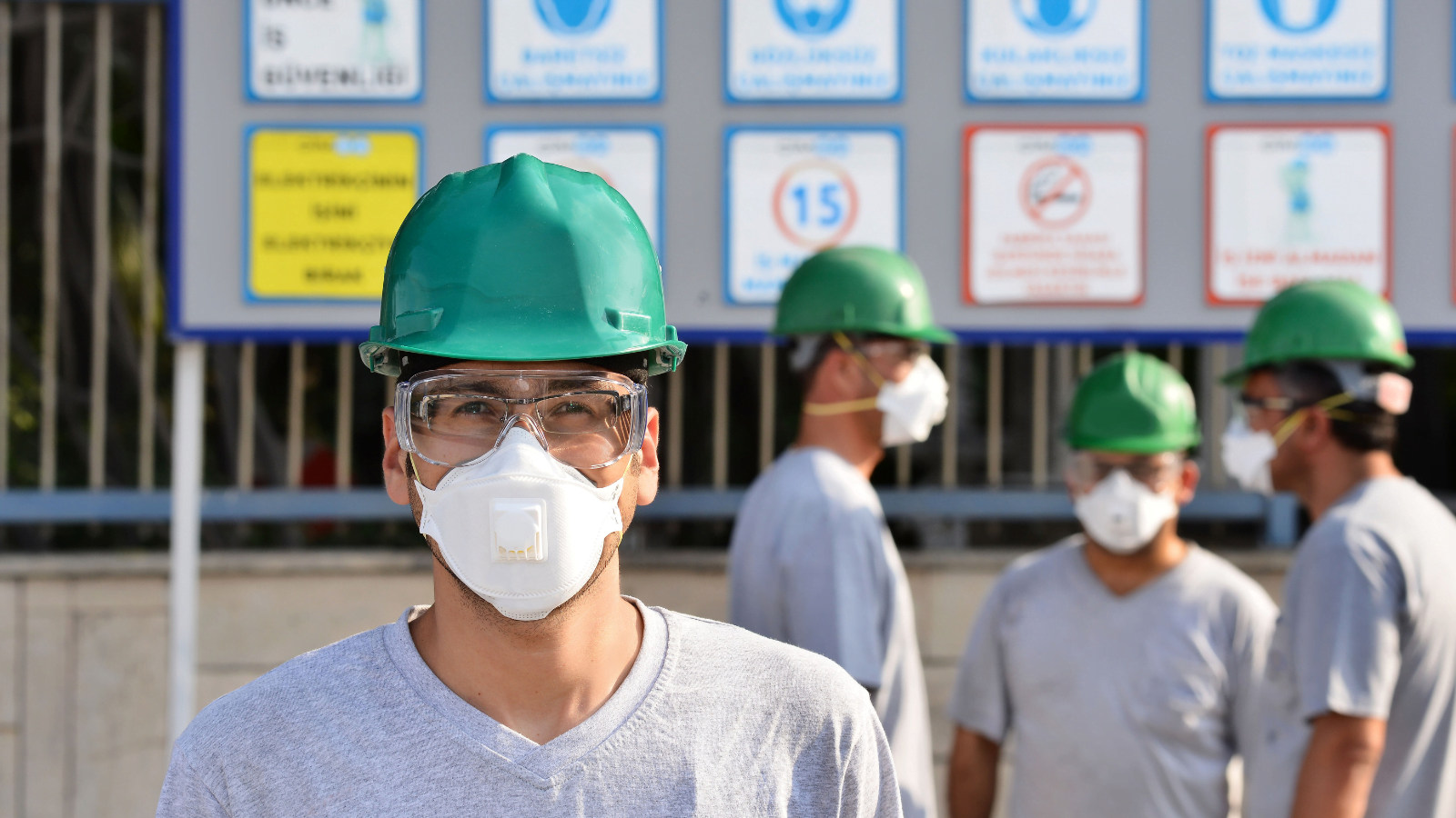 Four workmen wearing green hard hats and face masks to protect from construction dust.