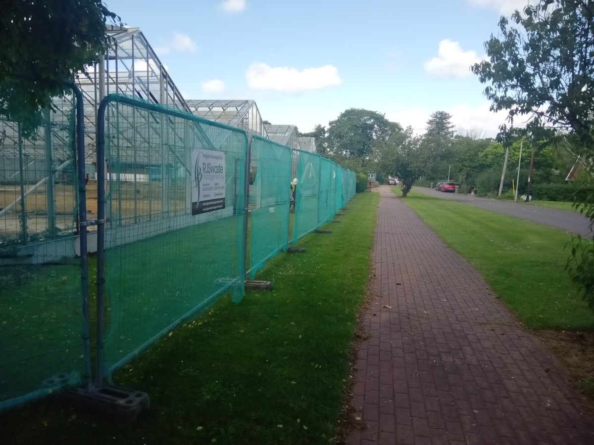 Heras fencing around showing RJS Waste Management sign around the Brinsbury College greenhouses demolition site